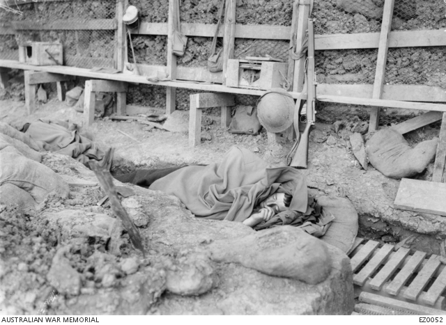 Wrapped in his overcoat, an unidentified Australian soldier sleeps in the trenches in the Bois Grenier sector. ©AWM EZ0052