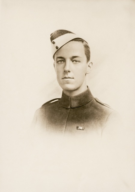 A studio portrait (head and shoulders) of a young man wearing a military cadet uniform, including cap