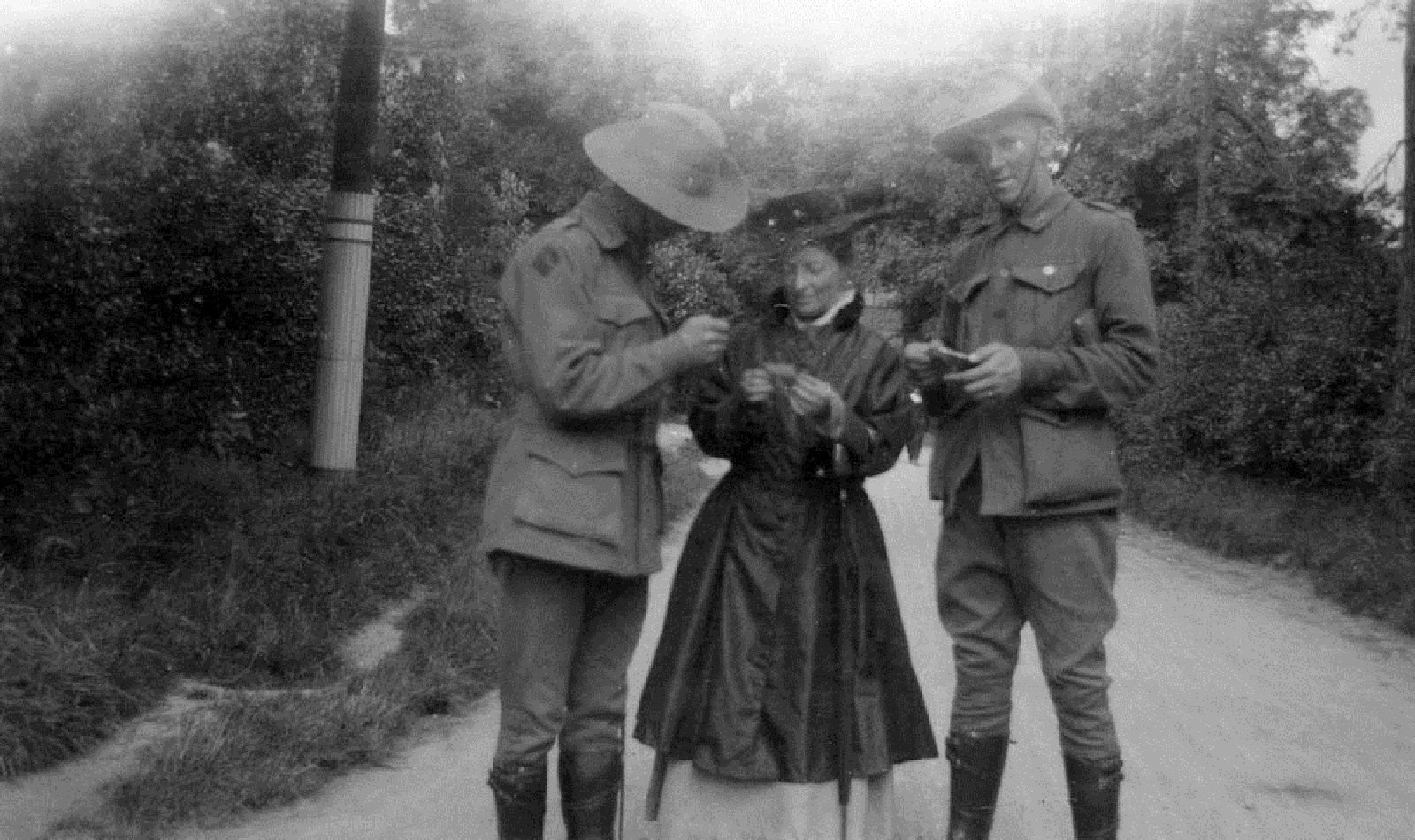 Two soldiers showing their photographs to a woman, all standing in a laneway