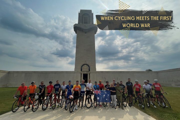 Cadel Evans' group of cyclists and the Director of the Sir John Monash Centre stand in front of the Australian National Memorial with an Australian flag.