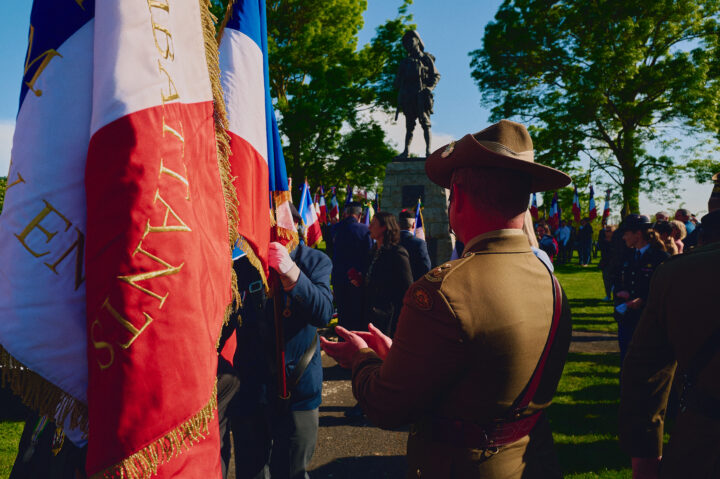 An Australian soldier wearing a slouch hat applauding a French flag bearer.